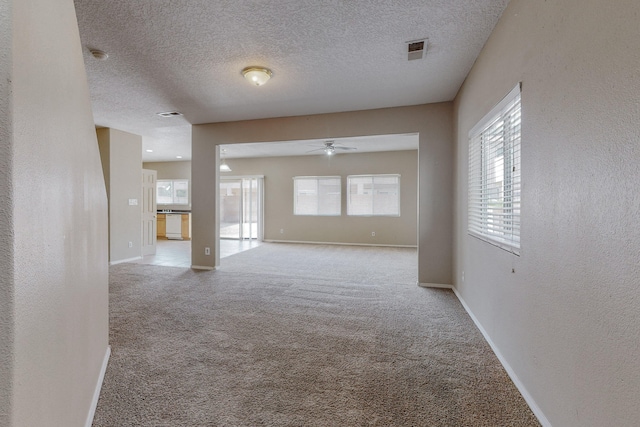 spare room with a textured ceiling, ceiling fan, and light carpet