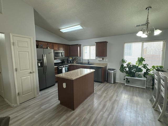 kitchen with a center island, sink, stainless steel appliances, an inviting chandelier, and decorative light fixtures