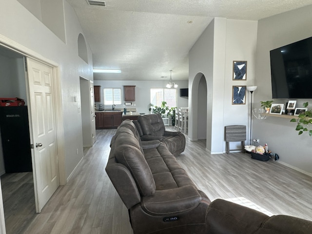 living room with sink, light wood-type flooring, a textured ceiling, and an inviting chandelier