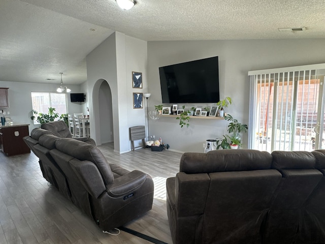 living room featuring a textured ceiling, light wood-type flooring, an inviting chandelier, and lofted ceiling