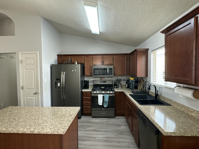 kitchen featuring backsplash, sink, vaulted ceiling, light wood-type flooring, and stainless steel appliances