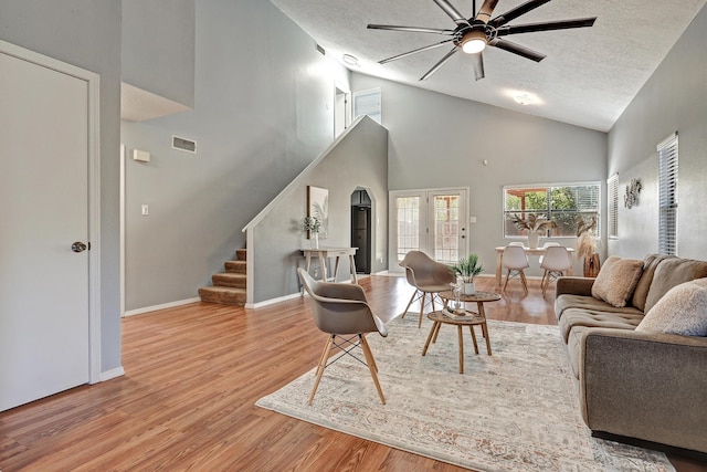 living room featuring ceiling fan, a textured ceiling, a high ceiling, and light hardwood / wood-style flooring