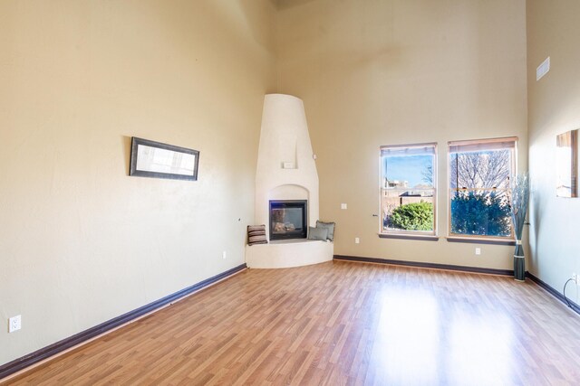 unfurnished living room featuring a large fireplace, a towering ceiling, and light hardwood / wood-style floors