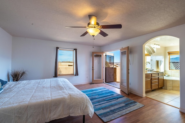 bedroom featuring ensuite bath, ceiling fan, french doors, light hardwood / wood-style floors, and a textured ceiling