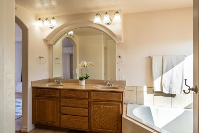 bathroom with tile patterned flooring, vanity, a textured ceiling, and tiled bath