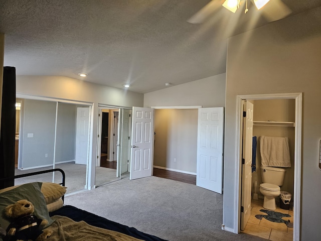 bedroom with multiple closets, ceiling fan, ensuite bathroom, carpet floors, and vaulted ceiling