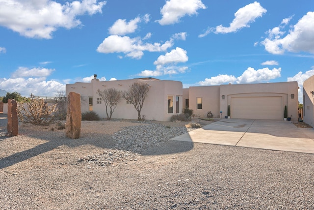 pueblo-style house with driveway, an attached garage, and stucco siding