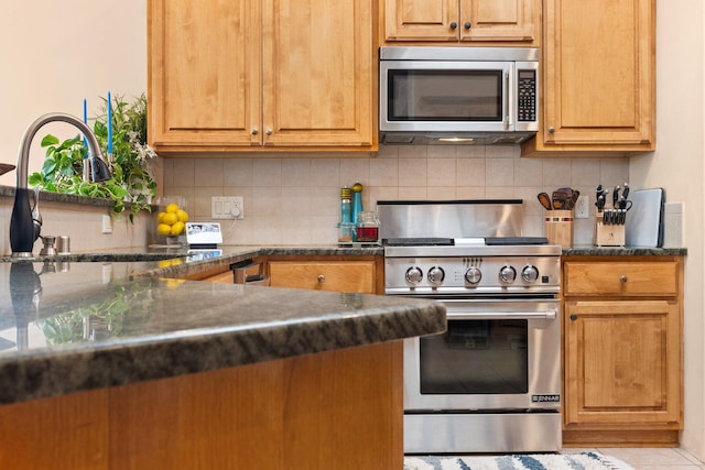 kitchen with stainless steel appliances, backsplash, dark countertops, and a sink