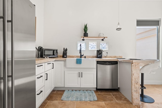 kitchen featuring stainless steel appliances, a sink, white cabinetry, stone finish floor, and pendant lighting