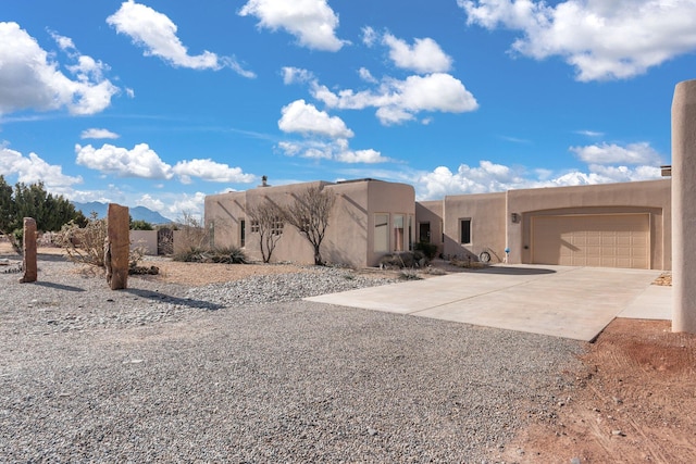 pueblo revival-style home featuring driveway, an attached garage, and stucco siding