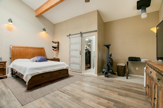 bedroom featuring light wood-type flooring, a walk in closet, a barn door, vaulted ceiling with beams, and a closet