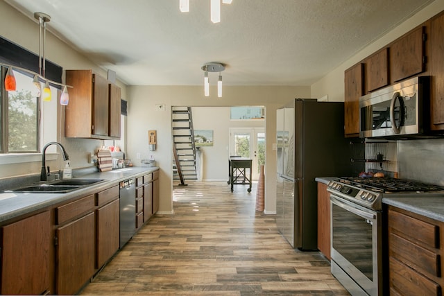 kitchen featuring a textured ceiling, stainless steel appliances, sink, decorative light fixtures, and light hardwood / wood-style floors