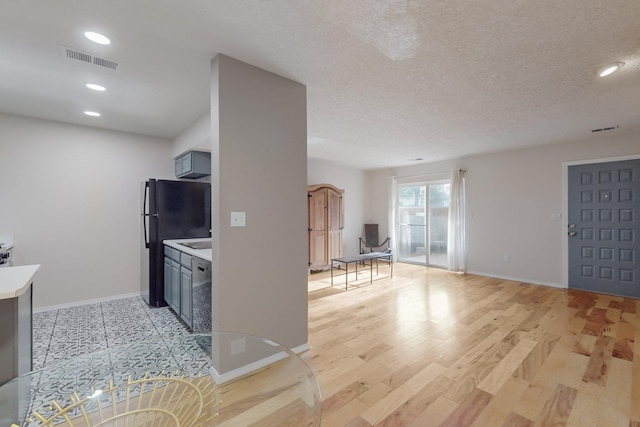 kitchen featuring gray cabinetry, black fridge, a textured ceiling, and light wood-type flooring