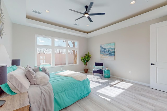 bedroom with ceiling fan, light hardwood / wood-style floors, and a tray ceiling