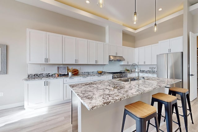 kitchen with an island with sink, appliances with stainless steel finishes, light stone countertops, white cabinets, and sink