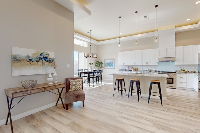 kitchen with a center island with sink, hanging light fixtures, stainless steel range, light stone countertops, and white cabinets