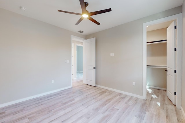 unfurnished bedroom with ceiling fan, a walk in closet, a closet, and light hardwood / wood-style flooring