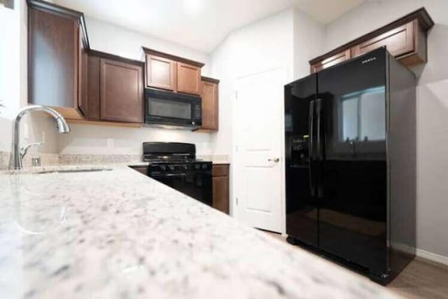 kitchen featuring sink, light stone counters, and black appliances