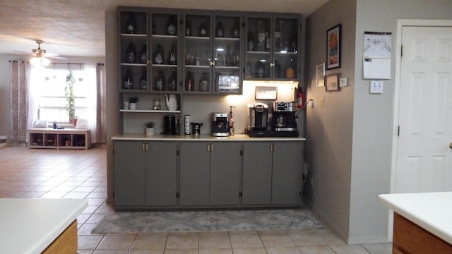 bar with gray cabinetry, a textured ceiling, ceiling fan, and light tile patterned floors