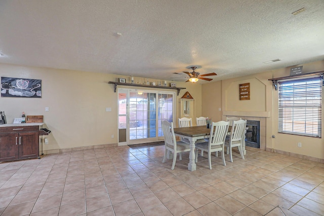 dining room featuring a tile fireplace, light tile patterned floors, a textured ceiling, and ceiling fan