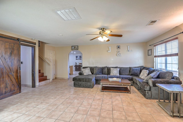 living room with ceiling fan, light tile patterned flooring, and a barn door