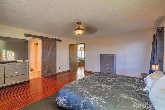 bedroom featuring a textured ceiling, ceiling fan, a barn door, and dark hardwood / wood-style floors