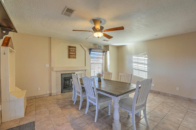 dining space with a tile fireplace, light tile patterned floors, a textured ceiling, and ceiling fan