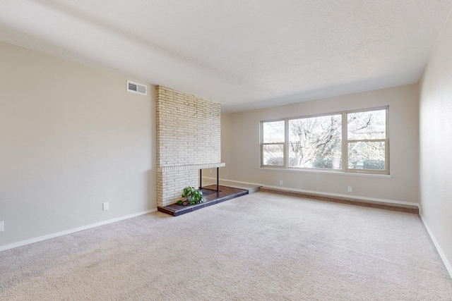 unfurnished living room with light colored carpet, a textured ceiling, and a brick fireplace