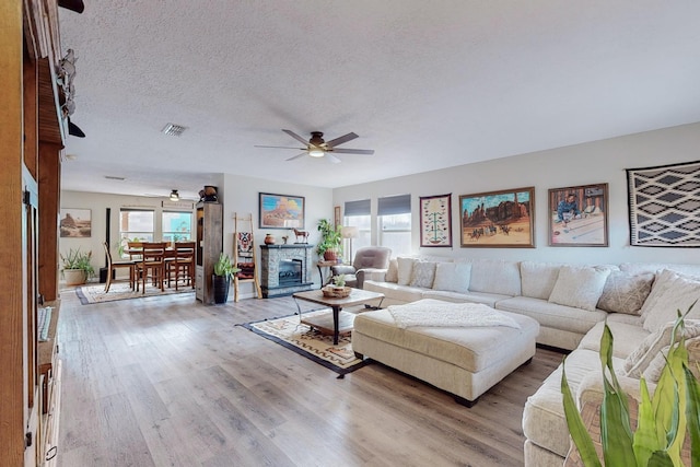 living room with ceiling fan, a textured ceiling, and light hardwood / wood-style flooring