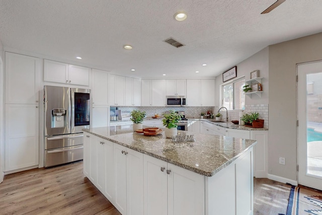 kitchen with white cabinets, appliances with stainless steel finishes, a center island, and light hardwood / wood-style floors