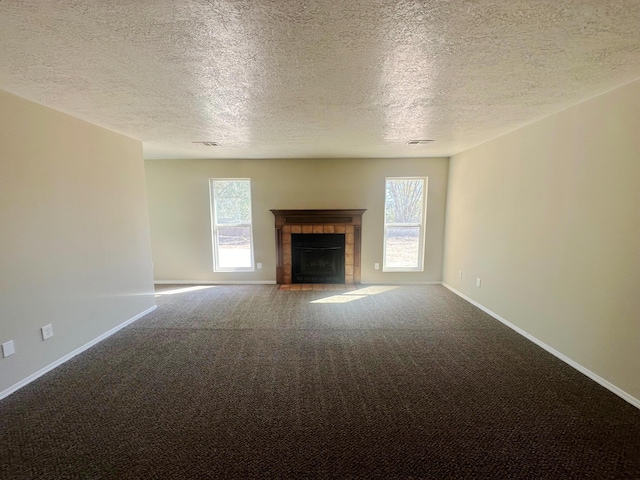 unfurnished living room with a fireplace, a textured ceiling, carpet floors, and a healthy amount of sunlight