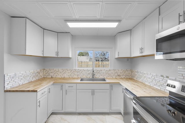 kitchen with butcher block counters, white cabinetry, sink, stainless steel appliances, and backsplash