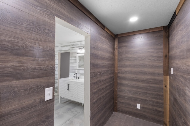 bathroom with wood walls, vanity, and a textured ceiling