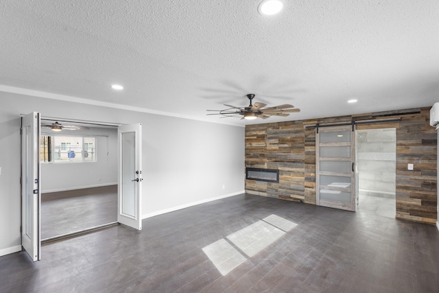 unfurnished living room featuring a wall mounted AC, a barn door, ceiling fan, and wood walls