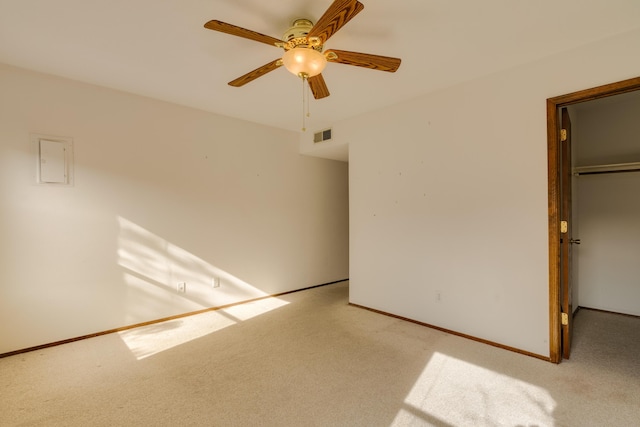 unfurnished bedroom with a walk in closet, a closet, light colored carpet, and ceiling fan