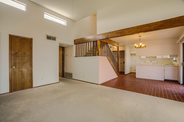 carpeted empty room with a chandelier, beam ceiling, a towering ceiling, and sink