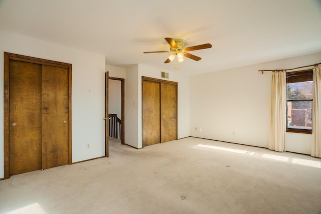 unfurnished bedroom with light colored carpet, ceiling fan, and multiple closets