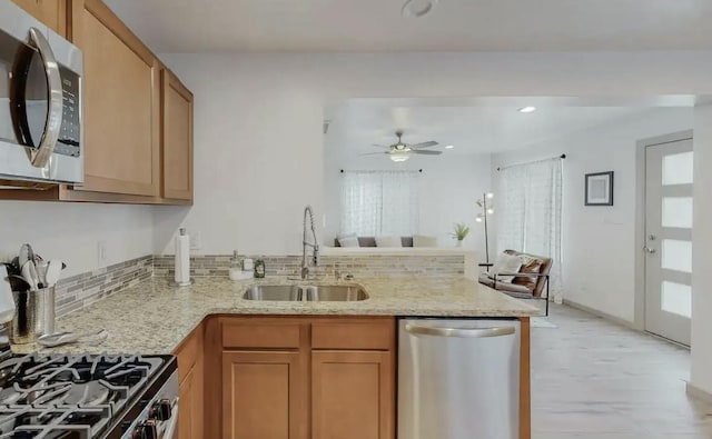 kitchen featuring kitchen peninsula, appliances with stainless steel finishes, light stone counters, ceiling fan, and sink