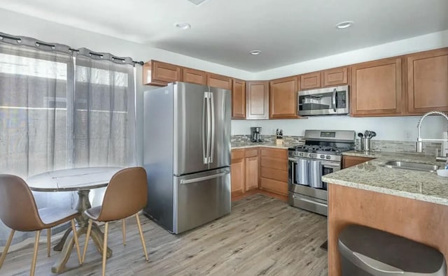 kitchen with light stone countertops, sink, light hardwood / wood-style floors, and appliances with stainless steel finishes