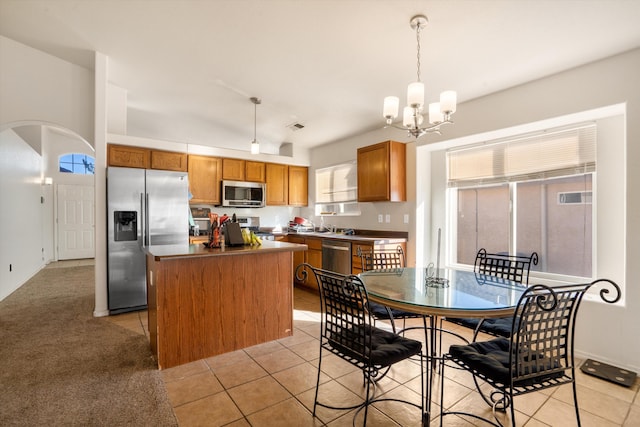 kitchen with a center island, arched walkways, light tile patterned floors, stainless steel appliances, and brown cabinetry