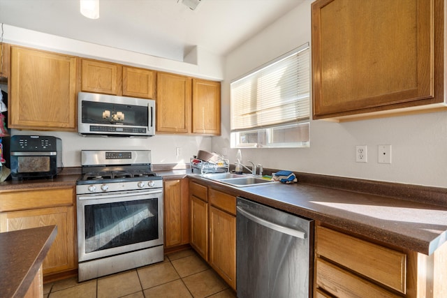 kitchen featuring light tile patterned floors, brown cabinetry, dark countertops, appliances with stainless steel finishes, and a sink