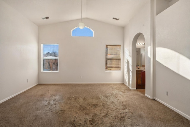 carpeted empty room featuring baseboards, visible vents, vaulted ceiling, and arched walkways