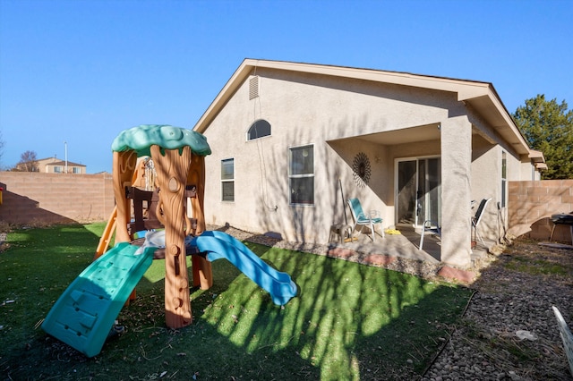 back of property featuring fence, a lawn, a playground, and stucco siding