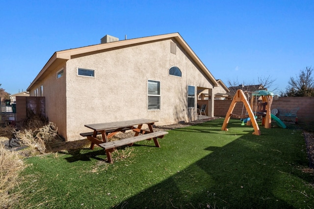 back of house with a playground, a yard, a fenced backyard, and stucco siding