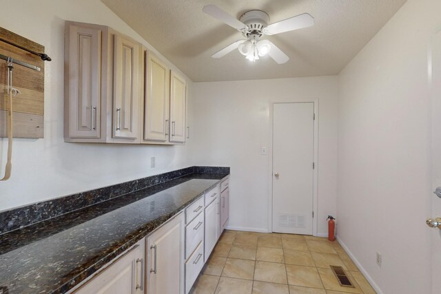 kitchen with ceiling fan, light tile patterned floors, dark stone counters, and a textured ceiling