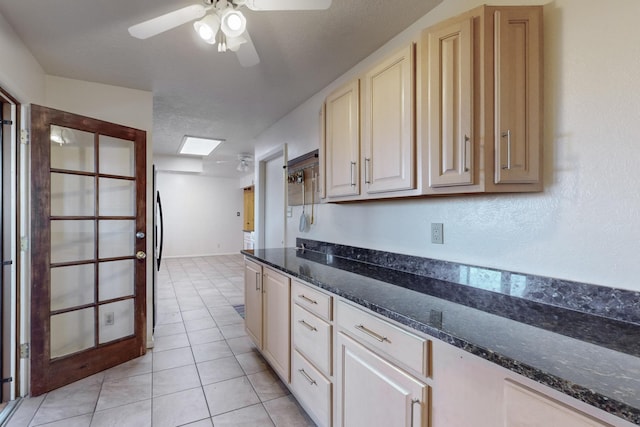 kitchen featuring a skylight, ceiling fan, dark stone counters, and light tile patterned flooring