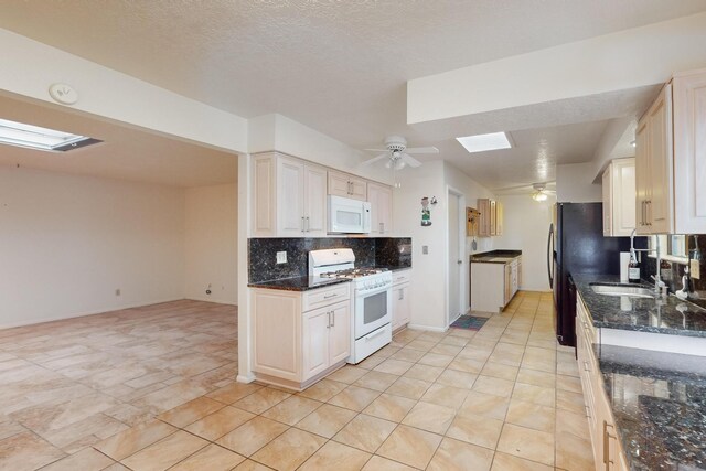 kitchen featuring backsplash, a skylight, dark stone counters, white appliances, and light tile patterned floors