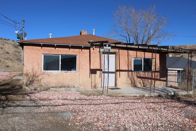 back of house with a chimney and stucco siding