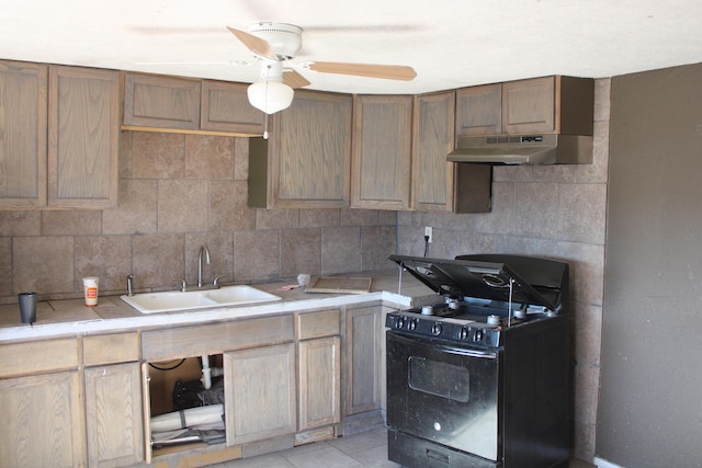 kitchen featuring under cabinet range hood, a sink, light countertops, decorative backsplash, and black gas range oven