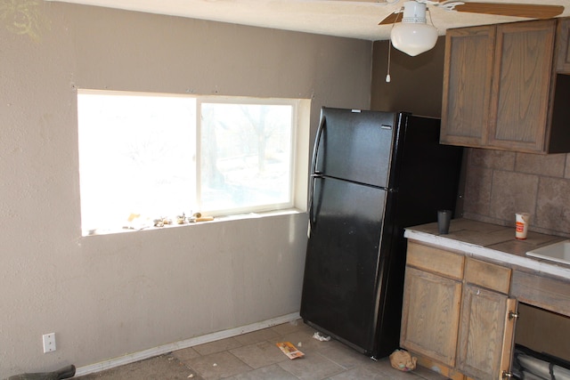 kitchen featuring baseboards, brown cabinets, freestanding refrigerator, light countertops, and backsplash